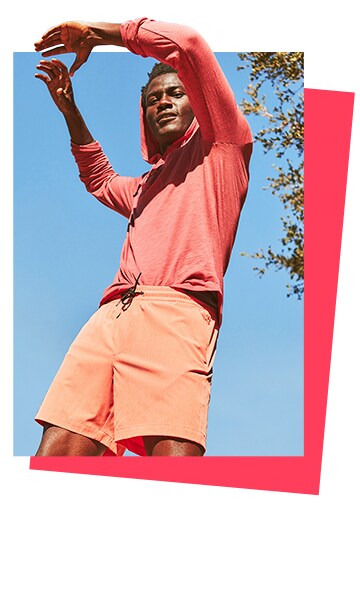A male model wearing a mauve sweatshirt and pale orange active shorts. 