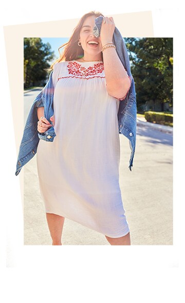 A female model in a white calf length dress with red embroidered detail around the neckline.