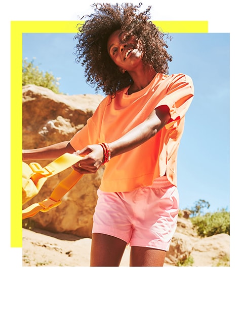 A female model wearing a bright orange tee paired with pastel pink shorts. 