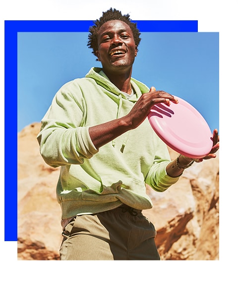 A male model wearing a neon green hoodie, khaki bottoms, and holding a frisbee.