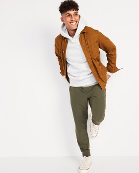 A model wears a brown activewear jacket, white hoodie and green Stretch Tech style joggers
