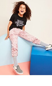 A  female model wearing a black t-shirt, tie-dye joggers, tall socks, and checkered slip on shoes. 