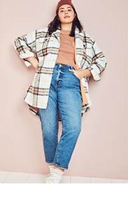 A female model  standing with her hands on her hips and wearing a beanie, an oversized cream flannel, and high-waisted jeans.