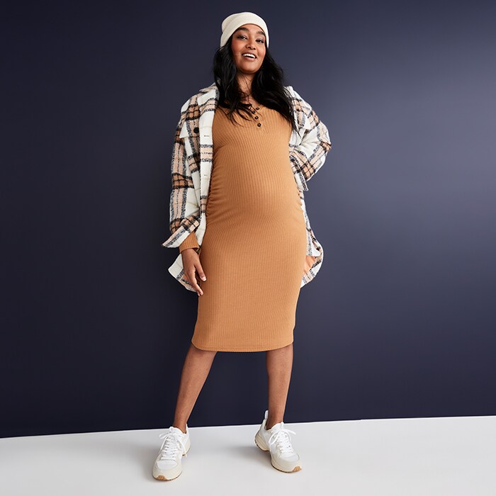 A maternity model wears a mohair colored maternity long-sleeve ribbed henley midi sweater dress and plaid coat