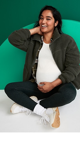 A maternity model wears a green sherpa zip-up fleece, a white t-shirt and green leggings