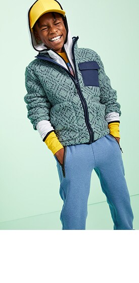 A male model wearing hoodies, active jacket, blue sweatpants and a yellow baseball cap.