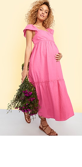 A maternity model wears a pink, short-sleeve maternity dress.