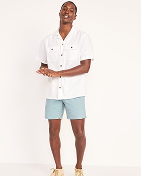 A male model wears a white short sleeve button-up shirt & light blue Lived-In khaki shorts.