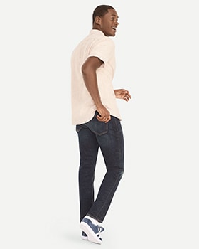 A male model wears dark washed Slim style jeans with a cream colored short sleeve shirt.