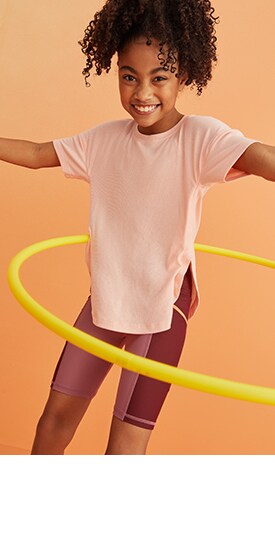 A female model dressed in active top and bike shorts using a hulahoop.