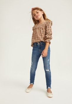 A female model wears Jegging style jeans with a plaid button up shirt.