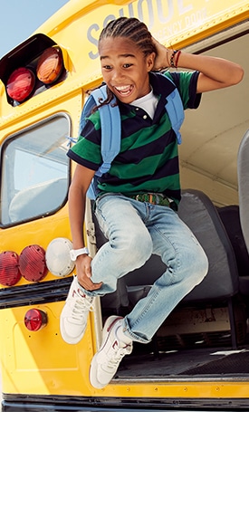 A young male model jumping from a school bus and wearing rugby-stripe jersey polo shirt and jeans.