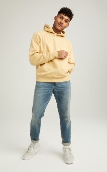 A male model wears Athletic Taper style jeans, & a light yellow hoodie