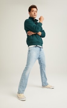 A male model wears Boot-Cut style jeans and a green pull-over sweatshirt