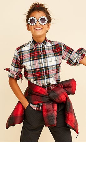 A young model wearing  plaid shirt for girls with sunglasses, black pants and plaid jacket tied around waist.