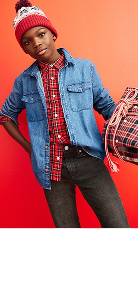 A young model wearing a denim shirt over a red plaid shirt with black jeans and a beanie cap.