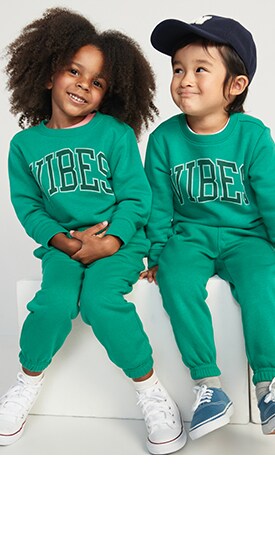 Two young models wearing green graphic sweatshirt and sweatpant sets.