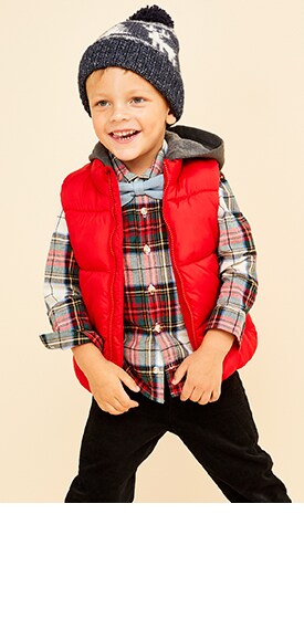 A young model wearing plaid shirt and red vest with skinny jeans and beanie cap.