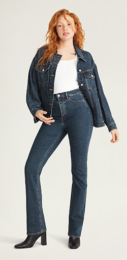 A model wearing a white tank, oversized jean jacket, and wide leg dark wash boot-cut jeans.
