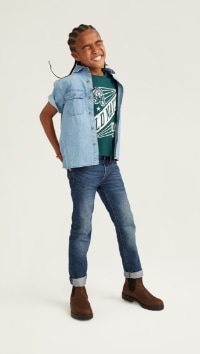 A male model wears Skinny style jeans with a short sleeve denim button up shirt over a graphic print t-shirt