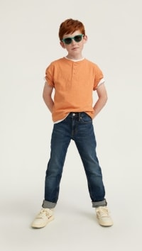 A male model wears Taper style jeans with an orange short sleeve t-shirt.