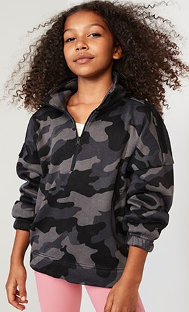 A young model dressed in a grey camouflage print quarter zip sweatshirt, paired with light pink active pants.