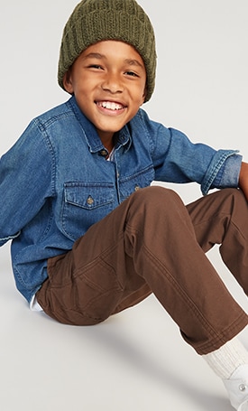 A boy dressed in brown chino pants, a denim buttondown shirt, and a beanie.
