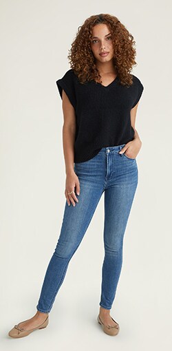 A model in a black blouse and light wash tapered blue jeans.