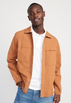 A male model wears a khaki colored long-sleeve button-up shirt over a white polo.