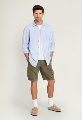 A male model wears a pair of dark green Relaxed Lived-In Cargo Shorts for Men -- 10-inch inseam & light blue long sleeve button up shirt