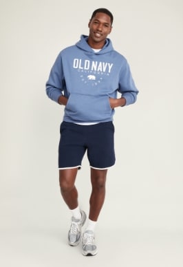 A male model wears a pair of dark blue Dolphin-Hem French Terry Shorts for Men -- 7-inch inseam & an Old Navy logo hoodie