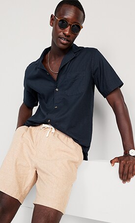 A male model wears a dark blue short sleeve button up shirt & light colored Linen-Blend Jogger Shorts for Men -- 7-inch inseam