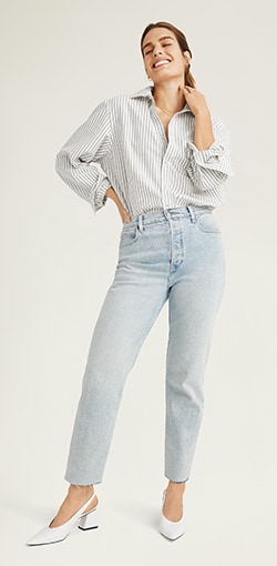 A model in a pair of light wash straight leg raw hem jeans.