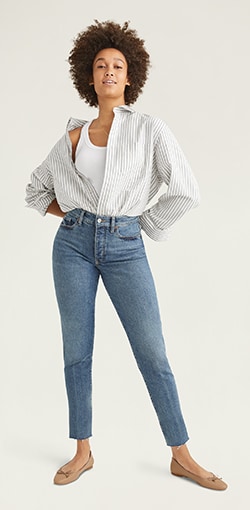 A female model in medium wash straight jeans with raw hem.