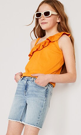 A female models wears an orange Ruffled Puckered-Jacquard Knit One-Shoulder Top & light wash denim shorts.