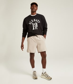 A male model wears a logo sweatshirt & light colored shorts.