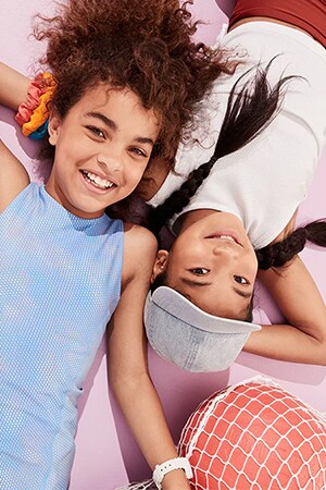Two young models laying down and wearing active tops, bottoms and baseball hat from Old Navy’s new arrivals collection.