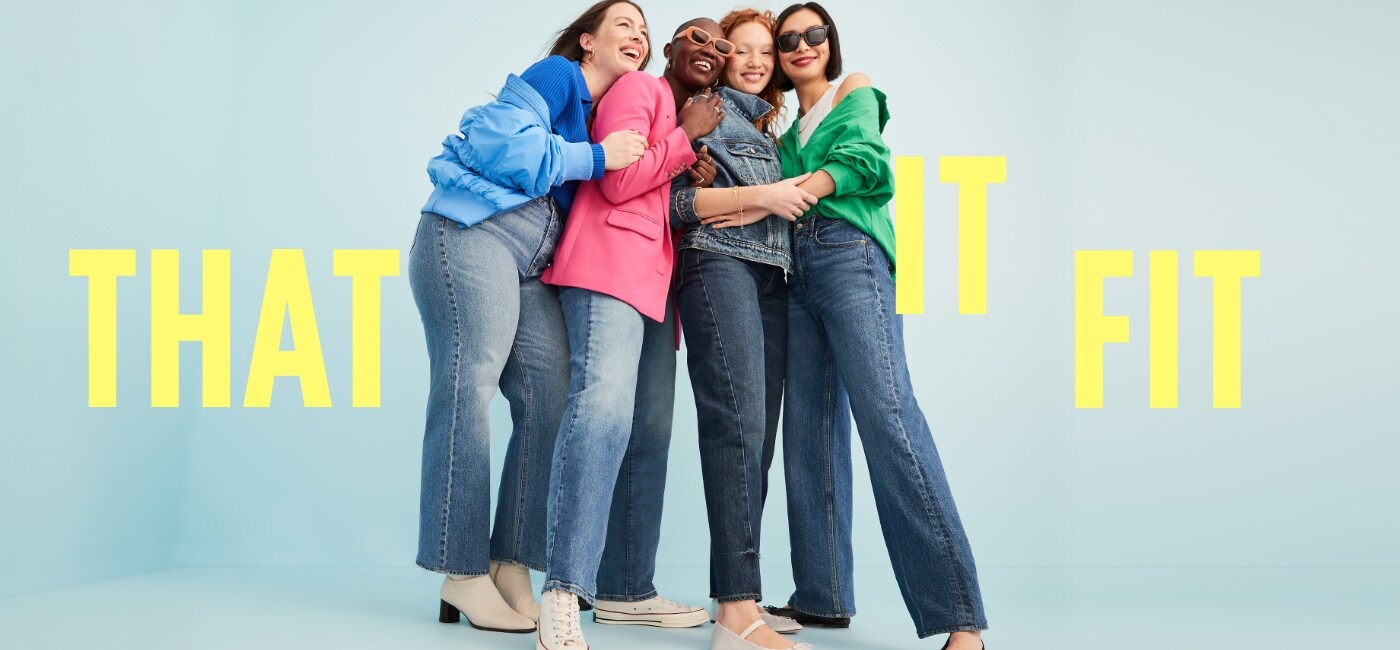Four female friends dressed in various shades and styles of denim jeans paired with bright pink, green, and blue tops and cardigans.
